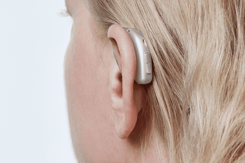 Audífono Oticon More, modelo miniRITE R, color Gris claro, foto tomada desde atrás en un ángulo de 45°, primer plano de la oreja, Mujer Audífonos con servicio ilimitado Auzen